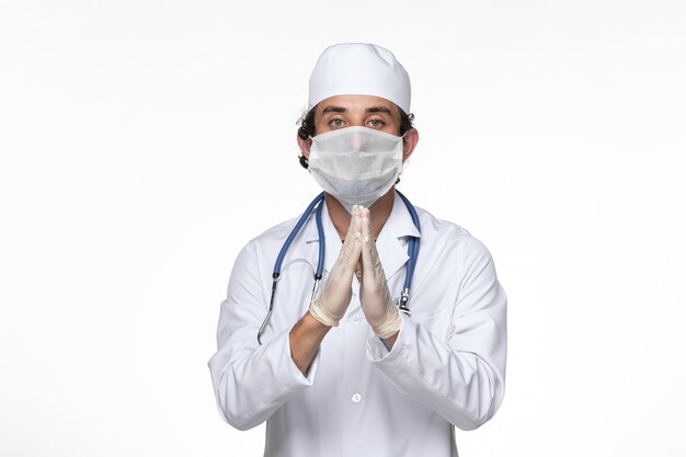 Vorderansicht männlicher Arzt im medizinischen Anzug, der eine sterile Maske als Schutz vor einer Covid-on-White-Desk-Virus-Krankheit trägt