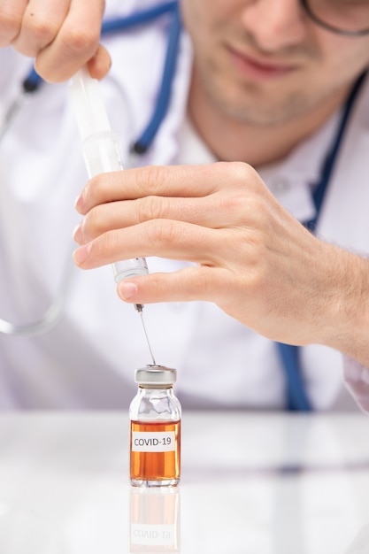 Vorderansicht männlicher Arzt im medizinischen Anzug, der Injektion mit Coronavirus-Impfstoff füllt