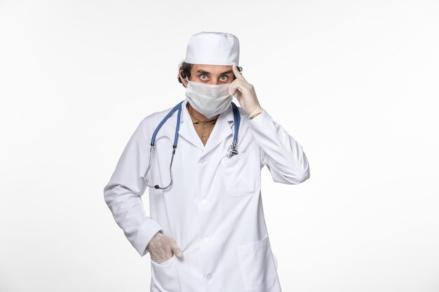Vorderansicht männlicher Arzt im medizinischen Anzug, der sterile Maske als Schutz vor Covid auf hellweißem Wandvirus-Coronavirus-Pandemie-Krankheitsgesundheit trägt