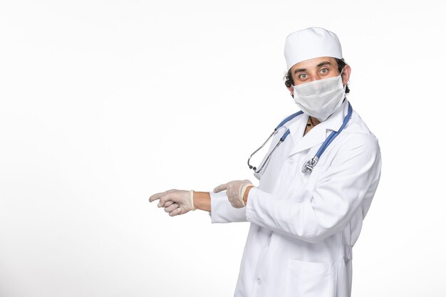 Vorderansicht männlicher Arzt im medizinischen Anzug, der sterile Maske als Schutz vor Covid auf Weißwand-Splash-Virus-Coronavirus-Pandemie trägt