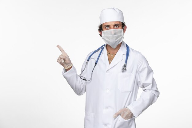Vorderansicht männlicher Arzt im medizinischen Anzug, der sterile Maske als Schutz vor Covid auf White Desk Virus Coronavirus Pandemie-Krankheit Krankheit trägt