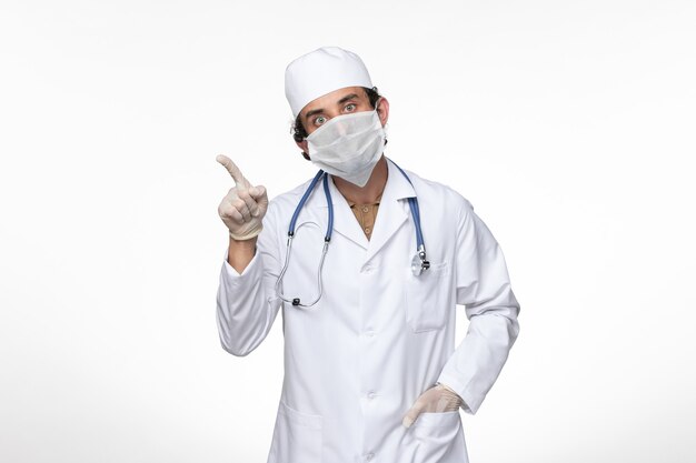 Vorderansicht männlicher Arzt im medizinischen Anzug mit steriler Maske als Schutz vor einer leicht weißen Wandvirus-Krankheit