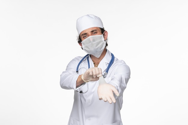 Vorderansicht männlicher Arzt im medizinischen Anzug mit steriler Maske als Schutz vor kovid tragenden Handschuhen auf der weißen Wand Virus Coronavirus Pandemie Krankheit Krankheit