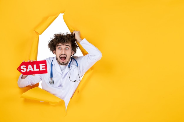 Vorderansicht männlicher Arzt im medizinischen Anzug mit Verkaufsschreiben auf gelbem Einkaufsmediziner in Farbe Gesundheitskrankenhaus