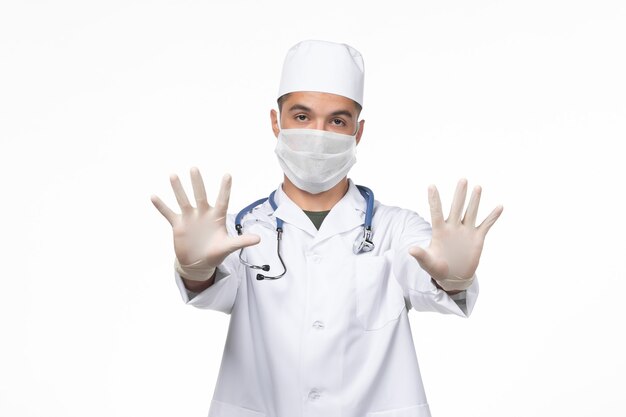 Vorderansicht männlicher Arzt im medizinischen Anzug und Maske gegen Coronavirus auf weißer Wand Covid-Virus-Krankheit Krankheit Isolationspandemie