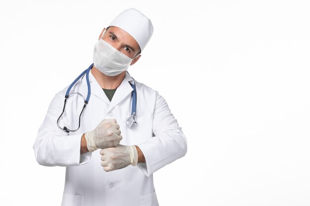 Vorderansicht männlicher Arzt im medizinischen Anzug und mit Maske aufgrund einer Covid-on-White-Wall-Covid-Virus-Pandemie-Virus-Krankheit