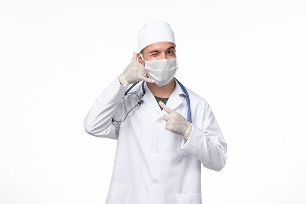 Vorderansicht männlicher Arzt im medizinischen Anzug und Tragen einer Maske gegen Covid auf dem weißen Schreibtisch Covid Disease Medicine Pandemic Virus