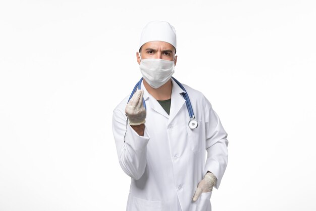 Vorderansicht männlicher Arzt im medizinischen Anzug und Tragen einer Maske gegen Covid auf weißem Schreibtisch Covid Disease Disease Pandemic Virus