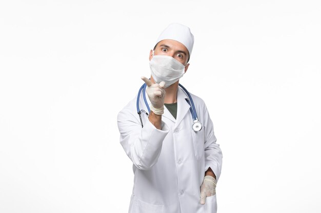 Vorderansicht männlicher Arzt im medizinischen Anzug und Tragen einer Maske gegen Covid auf weißem Schreibtisch Covid Disease Disease Pandemic Virus