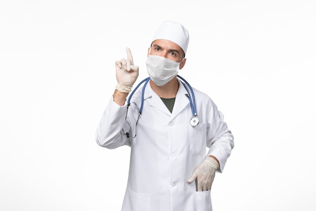 Vorderansicht männlicher Arzt im medizinischen Anzug und Tragen einer Maske gegen Covid auf weißer Wand Covid Disease Disease Pandemic Virus