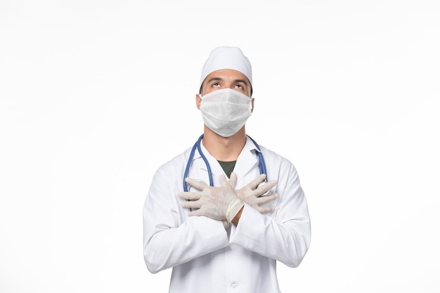 Vorderansicht männlicher Arzt im medizinischen Anzug und Tragen einer Maske gegen Covid auf weißer Wand Covid Virus Medizin Pandemie