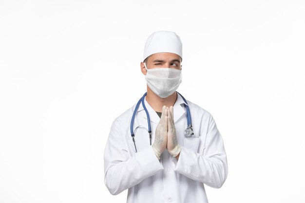 Vorderansicht männlicher Arzt im medizinischen Anzug und Tragen einer Maske gegen Covid auf weißer Wand Covid Virus Medizin Pandemie