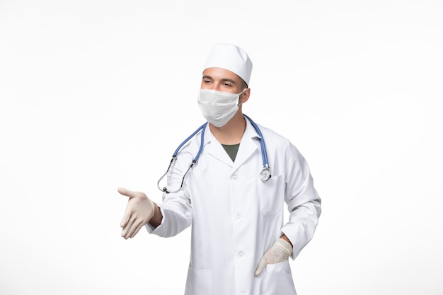 Vorderansicht männlicher Arzt im medizinischen Anzug und Tragen einer Maske gegen Covid Händeschütteln auf weißen Wand Covid Disease Disease Pandemic Virus