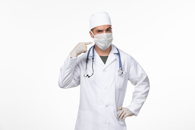 Vorderansicht männlicher Arzt im medizinischen Anzug und Tragen einer Maske gegen Covid Splash auf White Wall Virus Covid-Disease-Pandemie