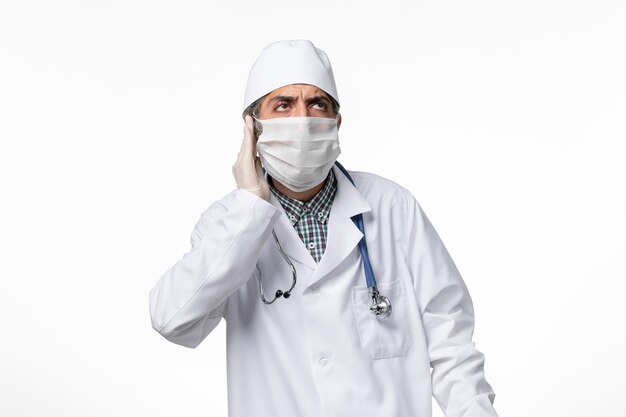 Vorderansicht männlicher Arzt im weißen medizinischen Anzug mit Maske wegen Coronavirus auf hellweißer Oberfläche