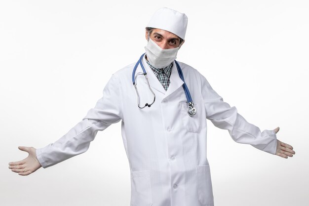 Vorderansicht männlicher Arzt im weißen medizinischen Anzug mit Maske wegen Covid auf White Floor Virus Covid-Krankheit Krankenhauspandemie