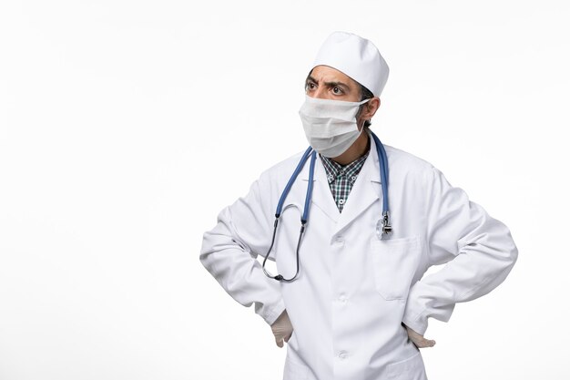 Vorderansicht männlicher Arzt im weißen medizinischen Anzug und in der Maske wegen Coronavirus auf hellweißer Oberfläche