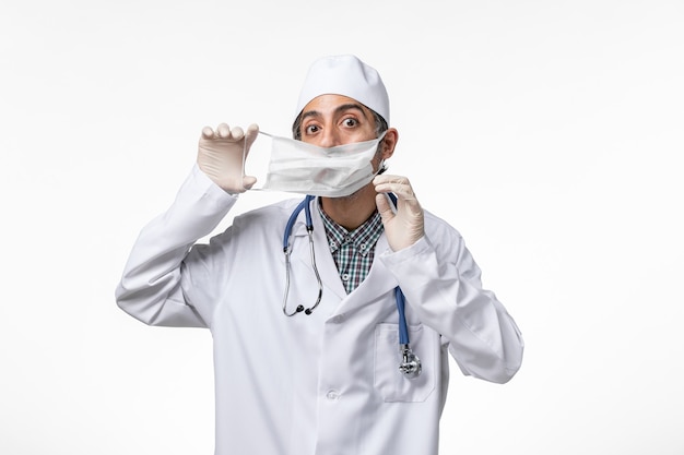 Vorderansicht männlicher Arzt im weißen medizinischen Anzug wegen Coronavirus, der Maske auf hellweißer Oberfläche trägt