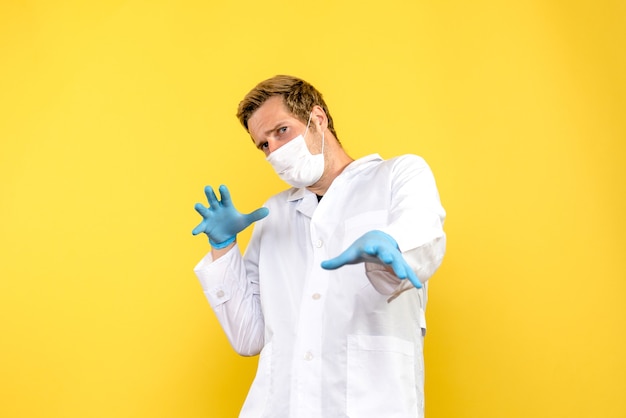 Vorderansicht männlicher Arzt in Maske auf gelbem Hintergrund covid Pandemie-Gesundheitsmediziner