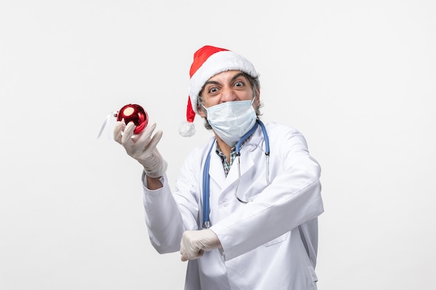 Vorderansicht männlicher Arzt in Maske mit Spielzeug auf weißem Boden Gesundheit Urlaub Covid Virus