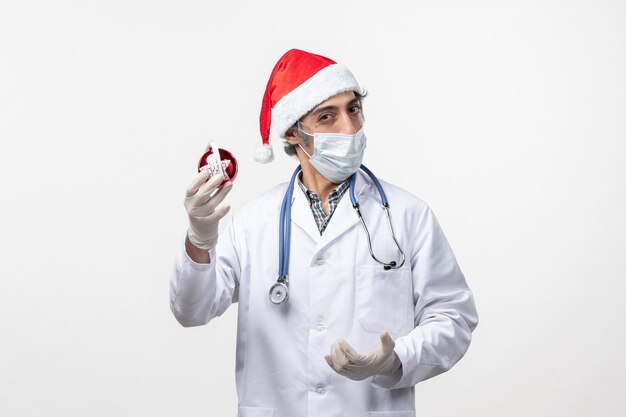 Vorderansicht männlicher Arzt in Maske mit Spielzeug auf weißem Wandgesundheitsfeiertags-Covid-Virus