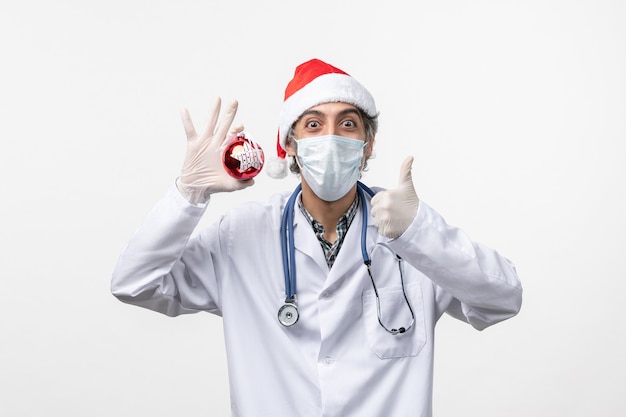Vorderansicht männlicher Arzt in Maske mit Spielzeug auf weißem Wandgesundheitsvirus covid neues Jahr