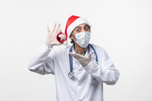 Vorderansicht männlicher Arzt in Maske mit Spielzeug auf weißer Wandvirus-Covid-Gesundheit