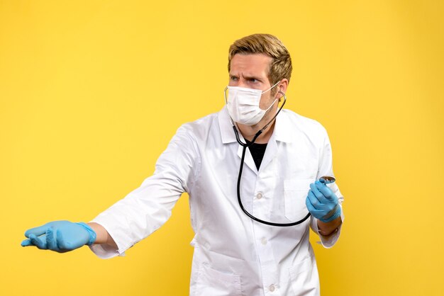 Vorderansicht männlicher Arzt in steriler Maske auf gelbem Hintergrund Pandemievirus covid Gesundheit