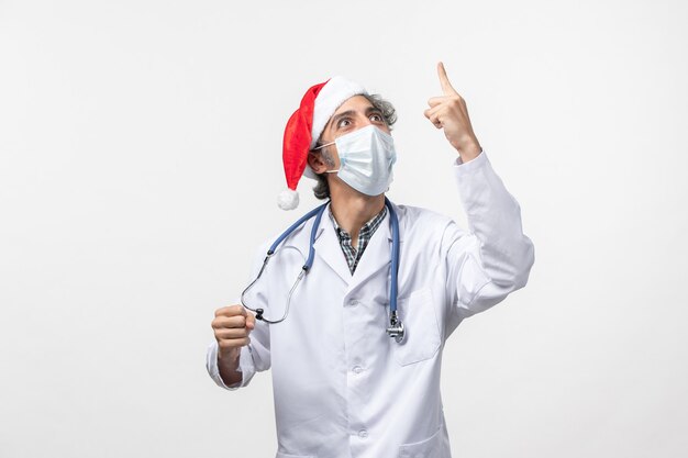 Vorderansicht männlicher Arzt in steriler Maske auf weißem Schreibtischvirus covid Neujahrsfeiertag