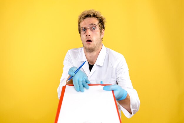 Vorderansicht männlicher Arzt mit Notizen auf gelbem Hintergrund Gesundheit Covid-Medic Mensch
