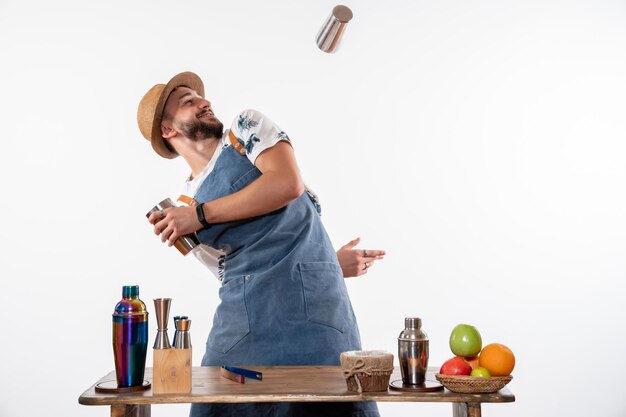 Vorderansicht männlicher Barkeeper, der einen Drink macht und mit Shakern an einer weißen Wand arbeitet