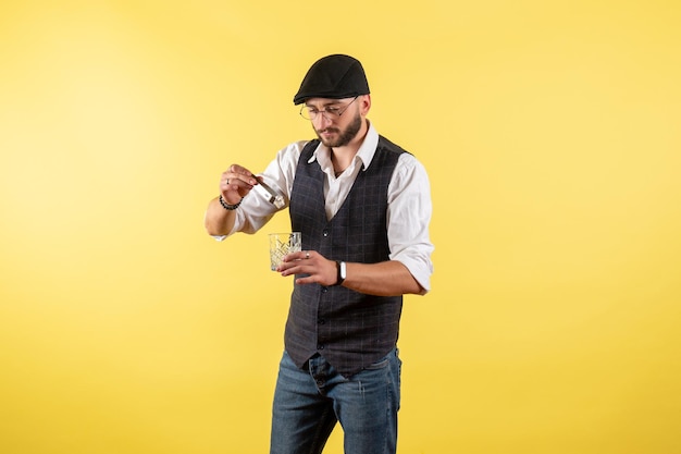 Vorderansicht männlicher Barkeeper, der Getränke mit Eiswürfeln auf gelber Wand macht, trinken Alkohol Job Nacht männliche Clubbar