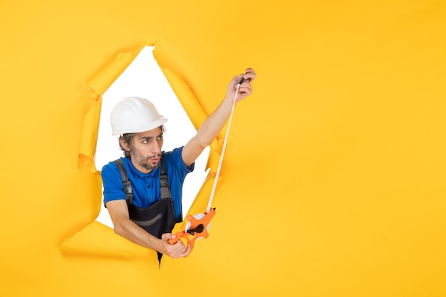 Vorderansicht männlicher Baumeister in Uniform mit Gerät auf gelber Wandfarbe Arbeiter Architektur Baukonstrukteur