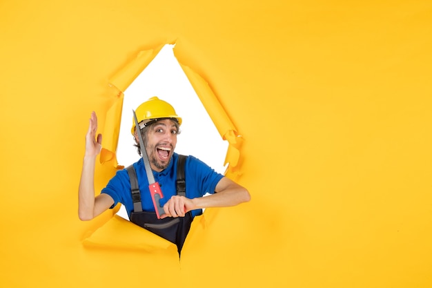 Vorderansicht männlicher Baumeister in Uniform mit Instrument in den Händen auf einem gelben Wandbau-Arbeitskraft-Auftragskonstrukteur