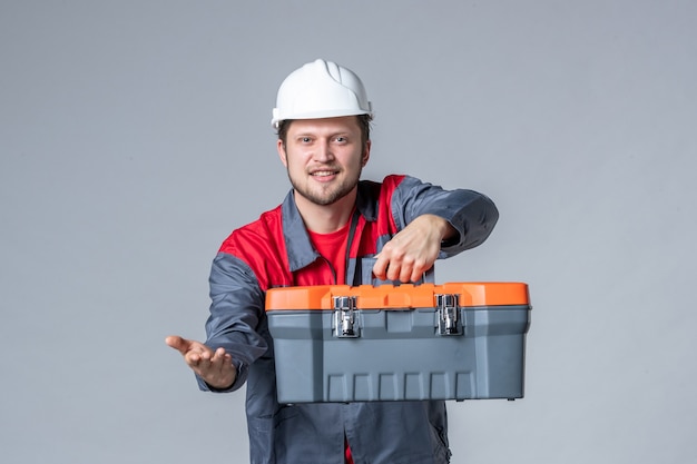 Vorderansicht männlicher Baumeister in Uniform mit Werkzeugkoffer auf grauem Hintergrund