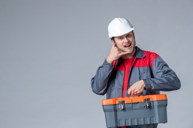 Vorderansicht männlicher Baumeister in Uniform mit Werkzeugkoffer auf grauem Hintergrund