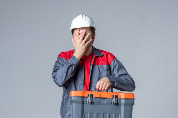 Vorderansicht männlicher Baumeister in Uniform mit Werkzeugkoffer auf grauem Hintergrund