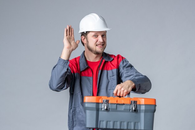 Vorderansicht männlicher Baumeister in Uniform mit Werkzeugkoffer auf grauem Hintergrund