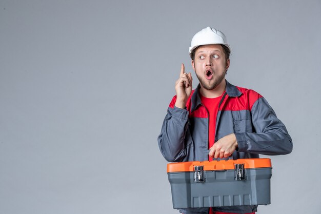 Vorderansicht männlicher Baumeister in Uniform mit Werkzeugkoffer hat eine Idee auf grauem Hintergrund