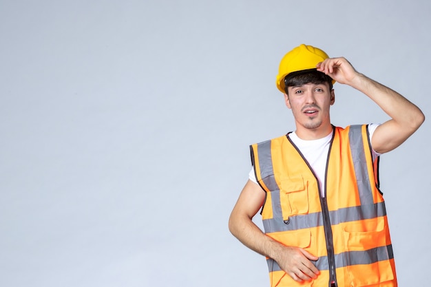 Vorderansicht männlicher Baumeister in Uniform und gelbem Helm auf grauer Wand