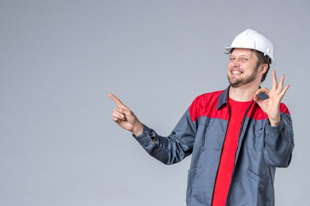 Vorderansicht männlicher Baumeister in Uniform und Helm auf grauem Hintergrund