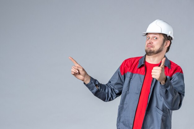 Vorderansicht männlicher Baumeister in Uniform und Helm auf grauem Hintergrund