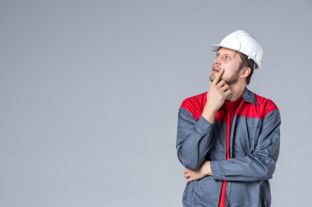 Vorderansicht männlicher Baumeister in Uniform und Helm auf grauem Hintergrund