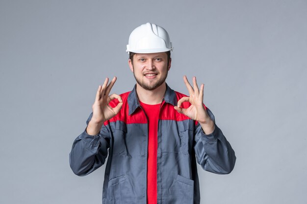 Vorderansicht männlicher Baumeister in Uniform und Helm auf grauem Hintergrund