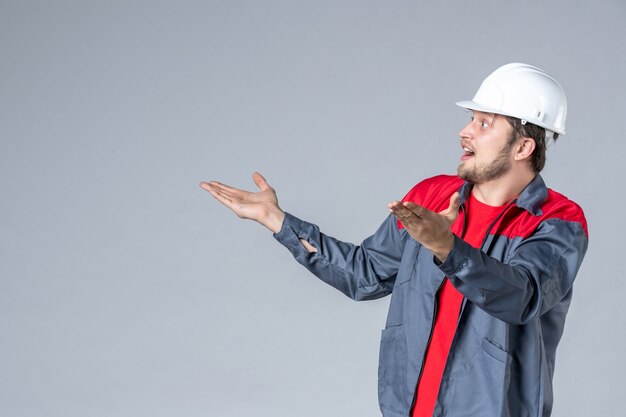 Vorderansicht männlicher Baumeister in Uniform und Helm auf grauem Hintergrund