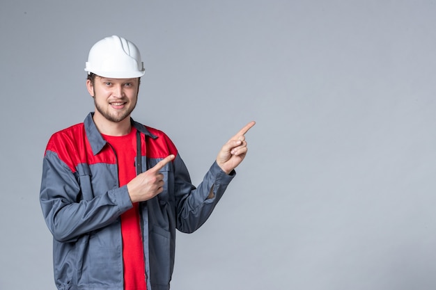 Vorderansicht männlicher Baumeister in Uniform und Helm auf hellem Hintergrund