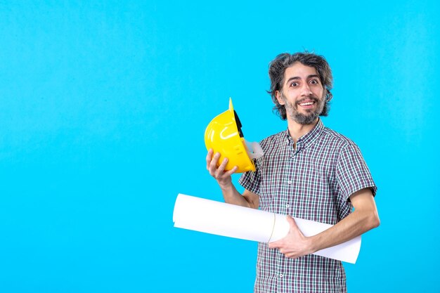 Vorderansicht männlicher Baumeister mit Plan auf seinen Händen auf blauem Hintergrund Ingenieur Konstrukteur Architektur Baujob Wolkenkratzer