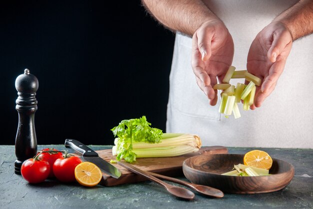 Vorderansicht männlicher Koch, der Sellerie auf dunkler Wandsalatdiätmahlzeit-Foto-Lebensmittelfarben kocht, die Küche kocht