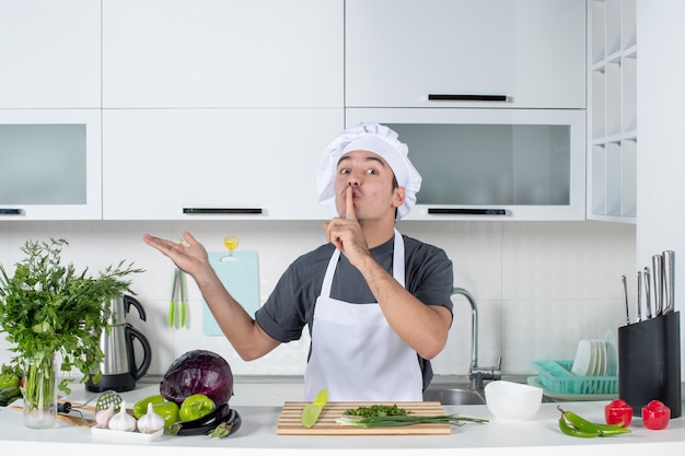 Vorderansicht männlicher Koch in Uniform, der ein Hush-Schild hinter dem Küchentisch macht
