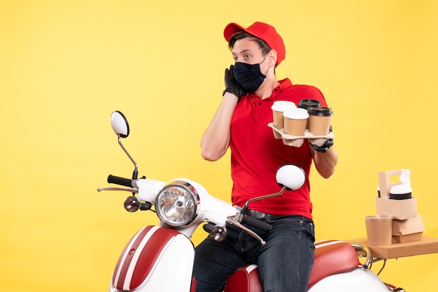 Vorderansicht männlicher Kurier auf Fahrrad in Maske mit Kaffee auf Gelb